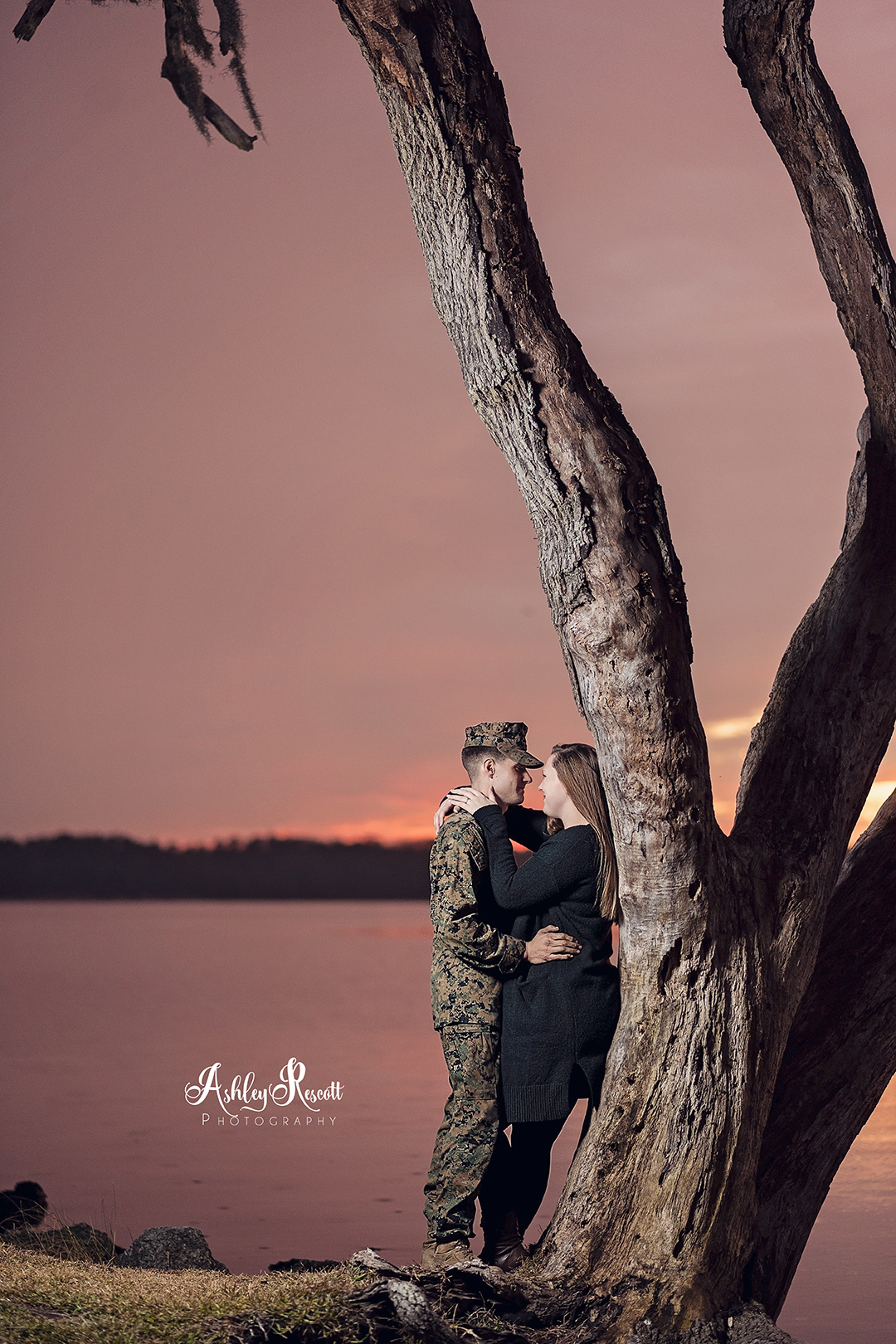 couple leaning on tree at sunset next to water