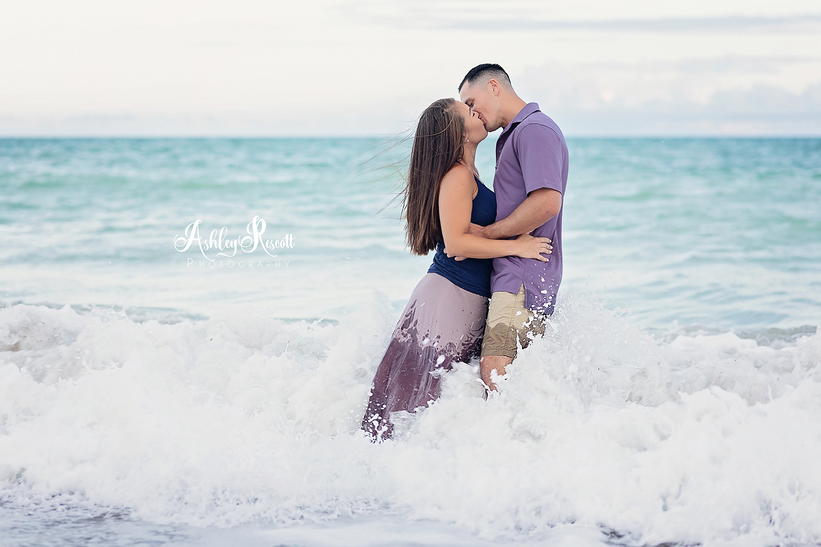 couple kissing while standing in waves at beach at sunset