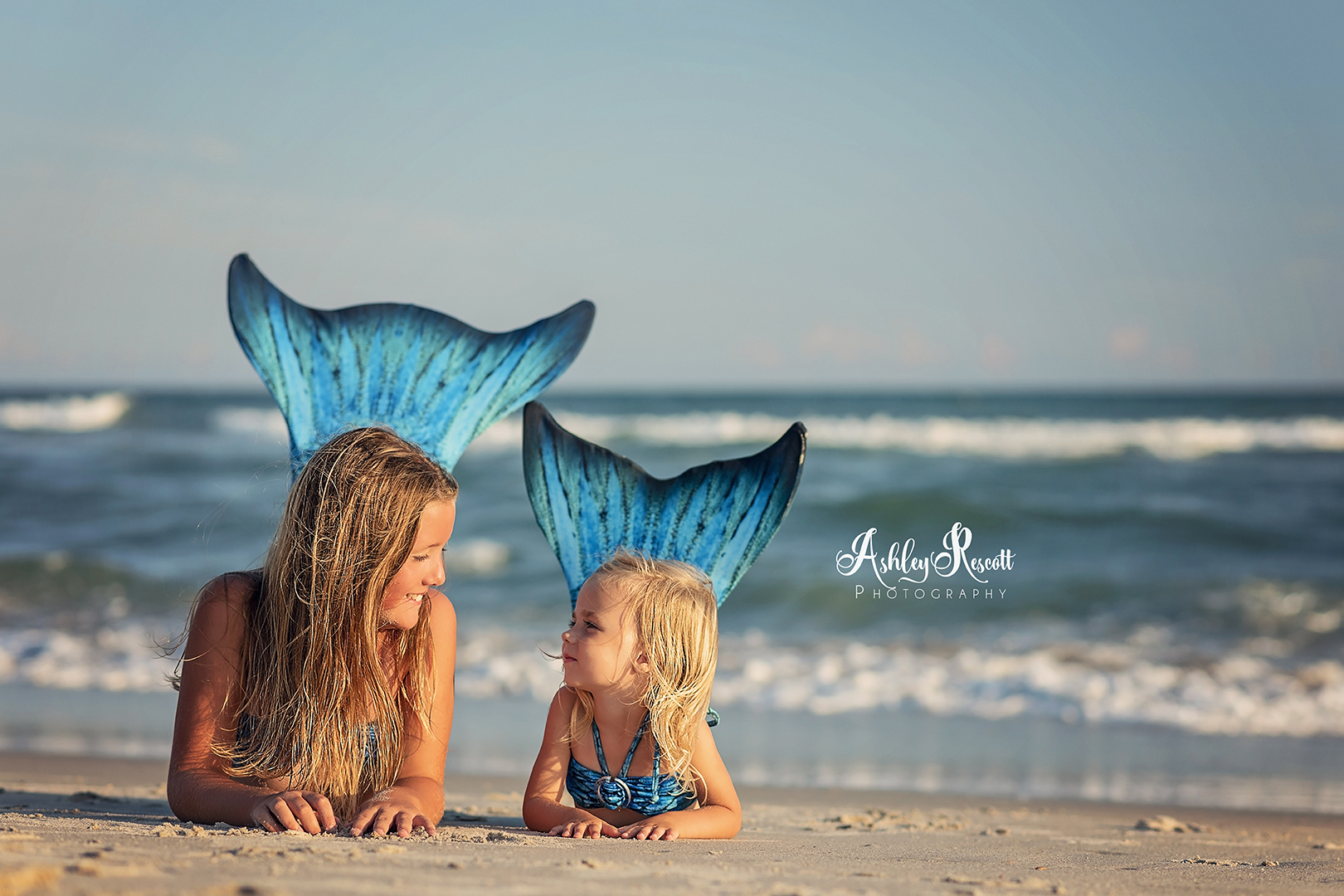 sisters in mermaid tails on beach