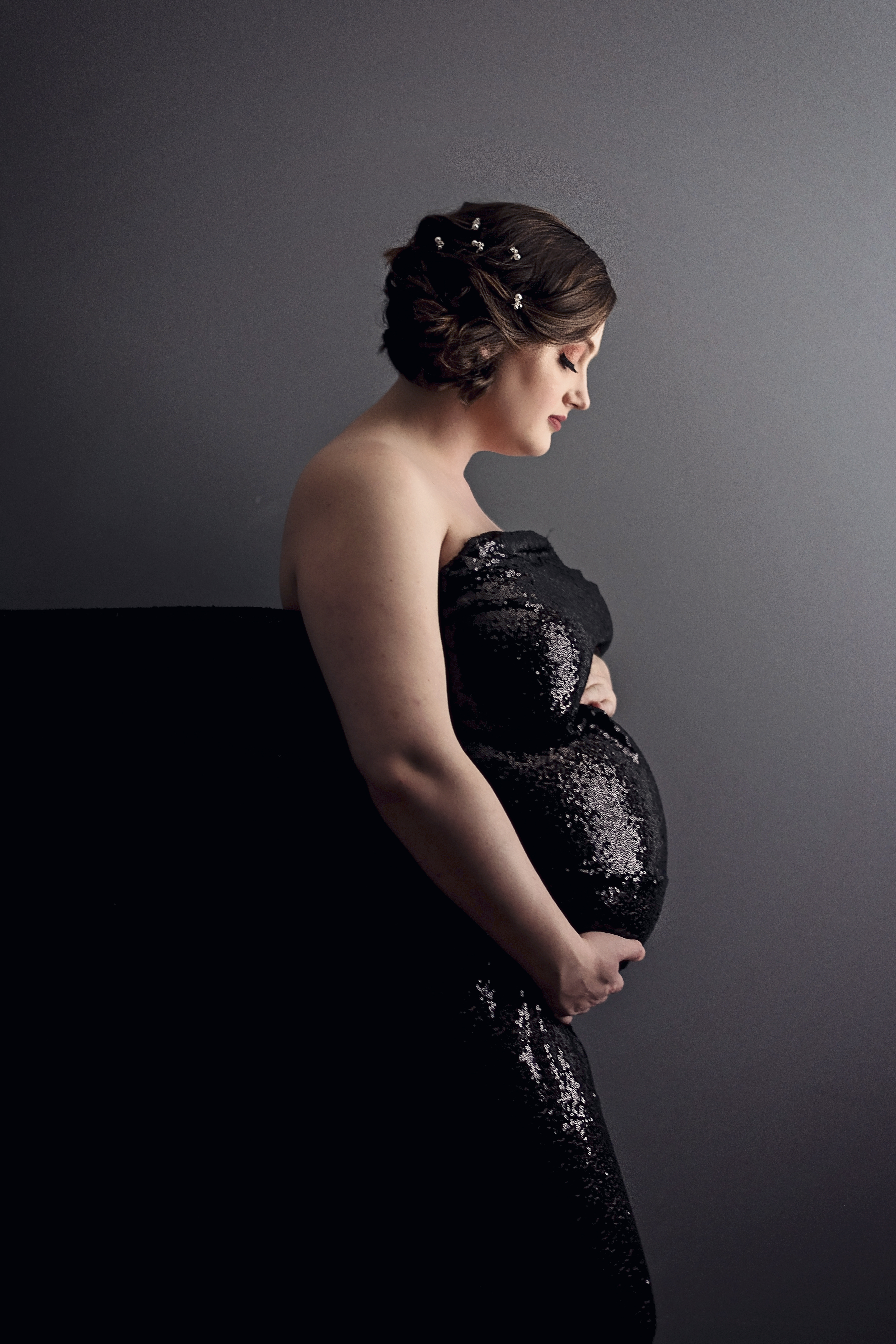 pregnant woman wrapped in black sequins looking at baby belly