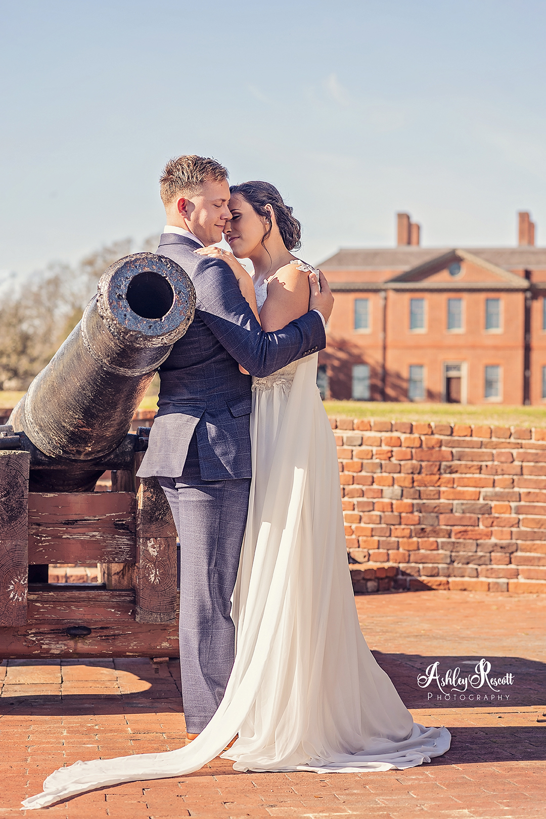 bride & groom leaning against cannon with tryon palace in the background