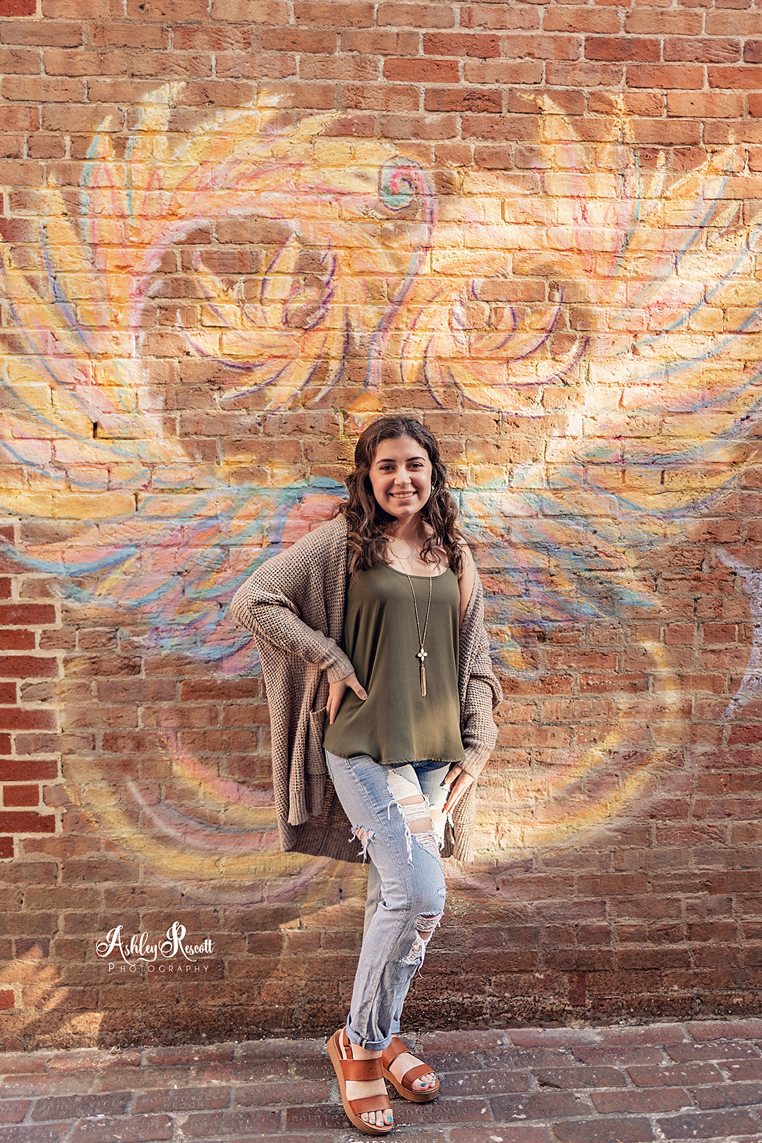 teen girl standing in front of chalk drawn wings on brick wall