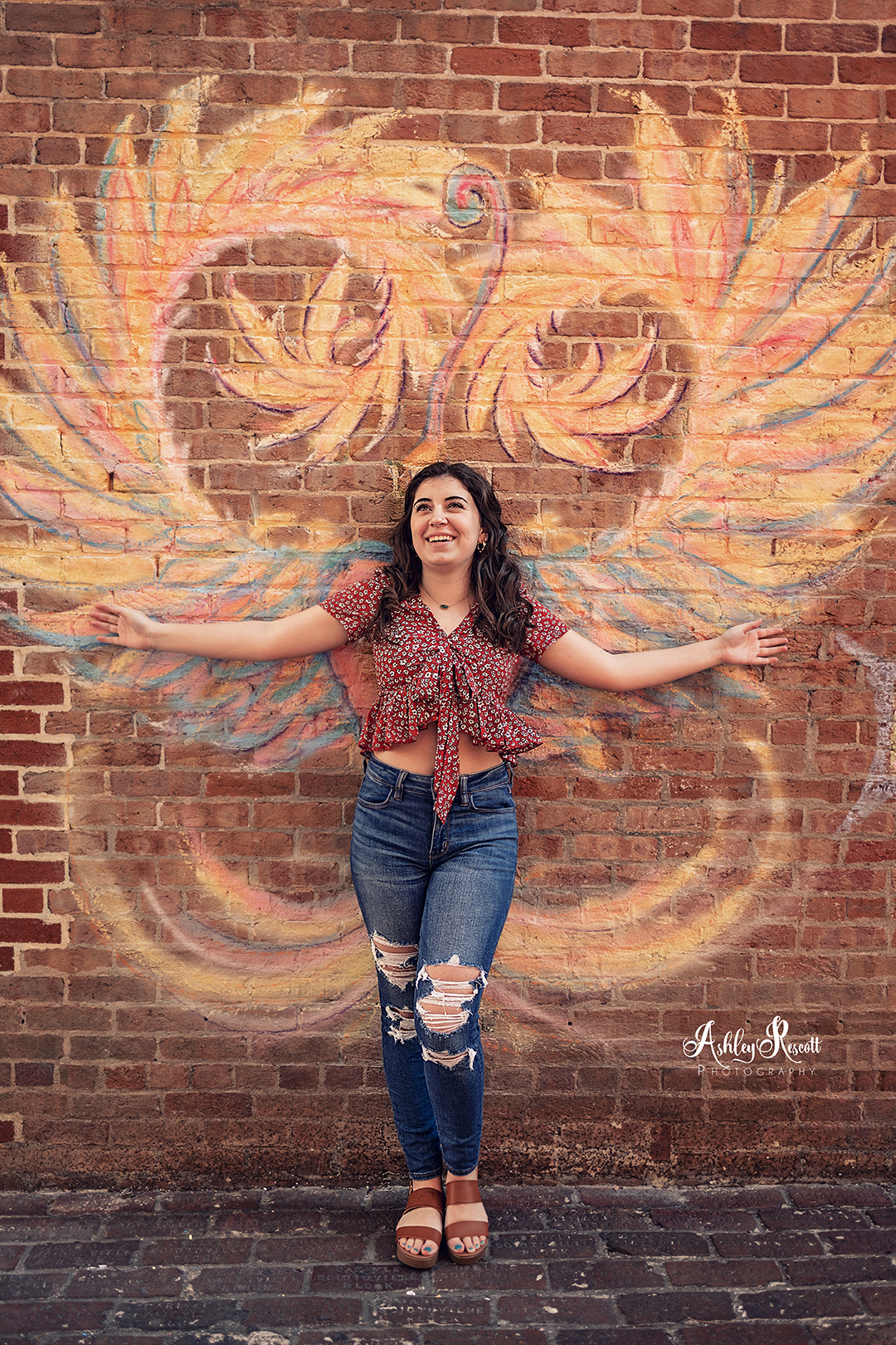 teen girl standing in front of chalk drawn wings on brick wall