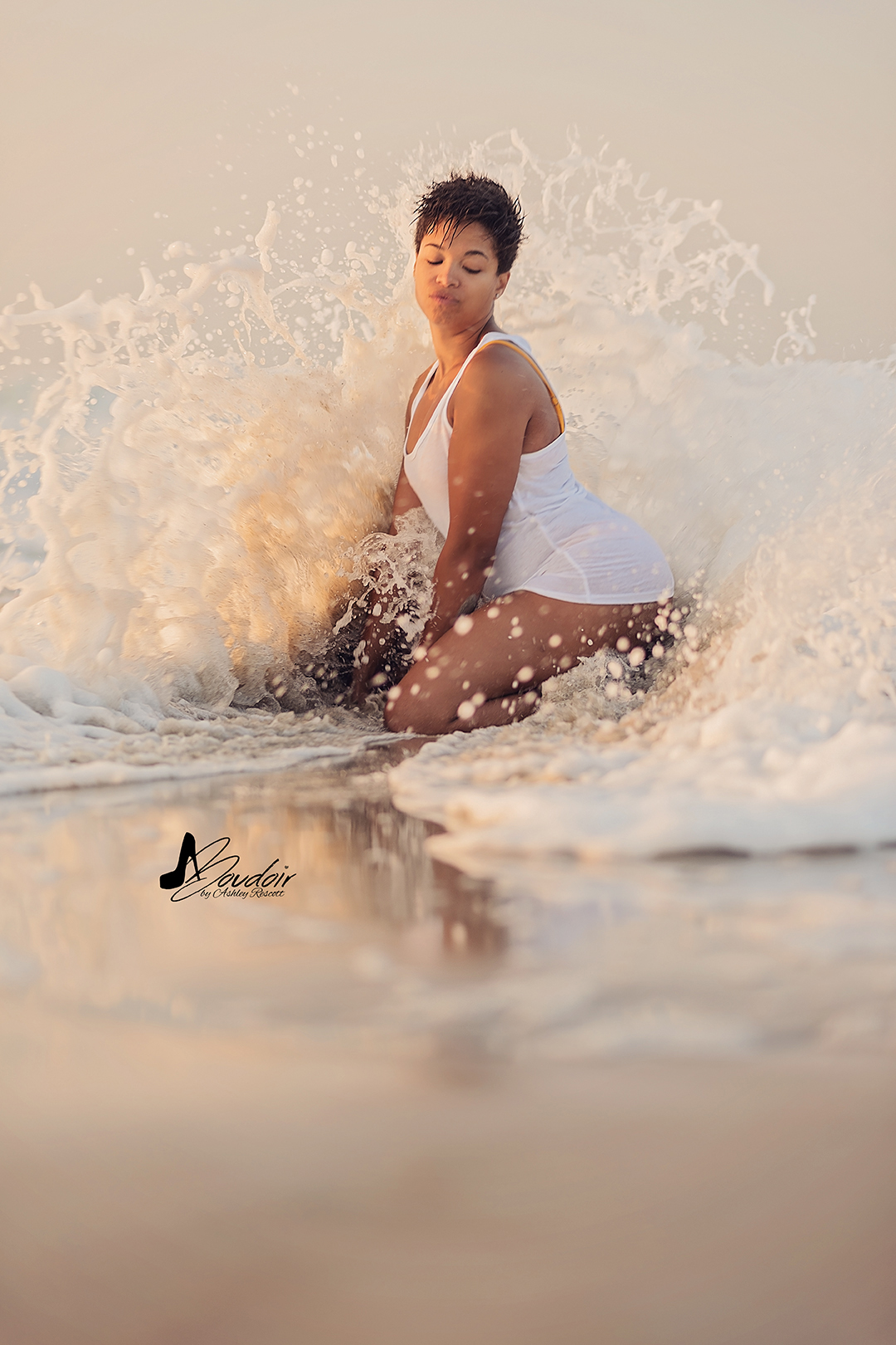 woman kneeling in white tank top on beach being hit by a wave